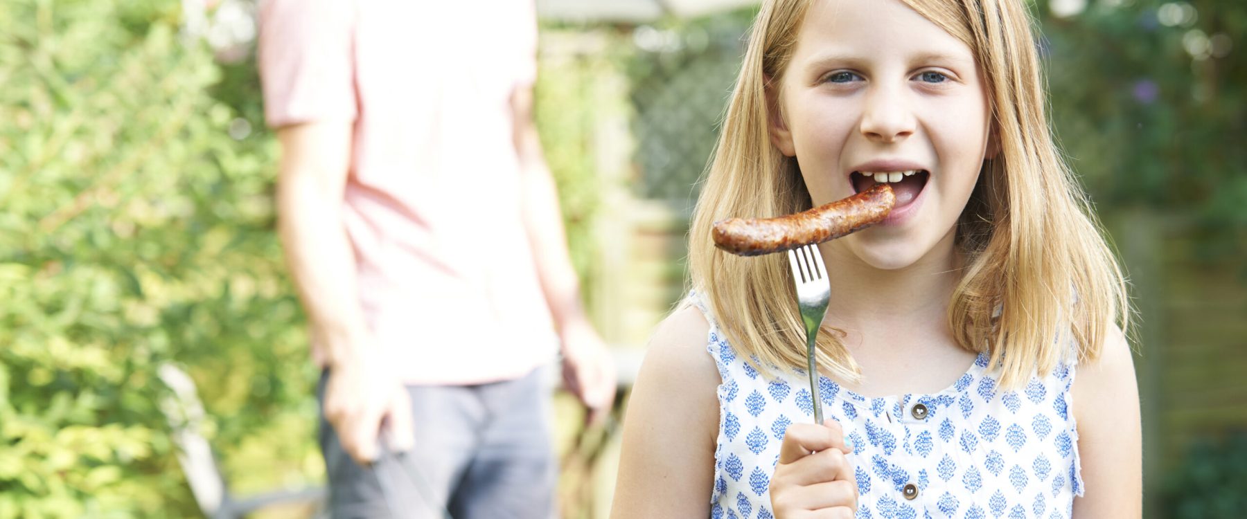 Girl Eating Sausage At Family Barbeque